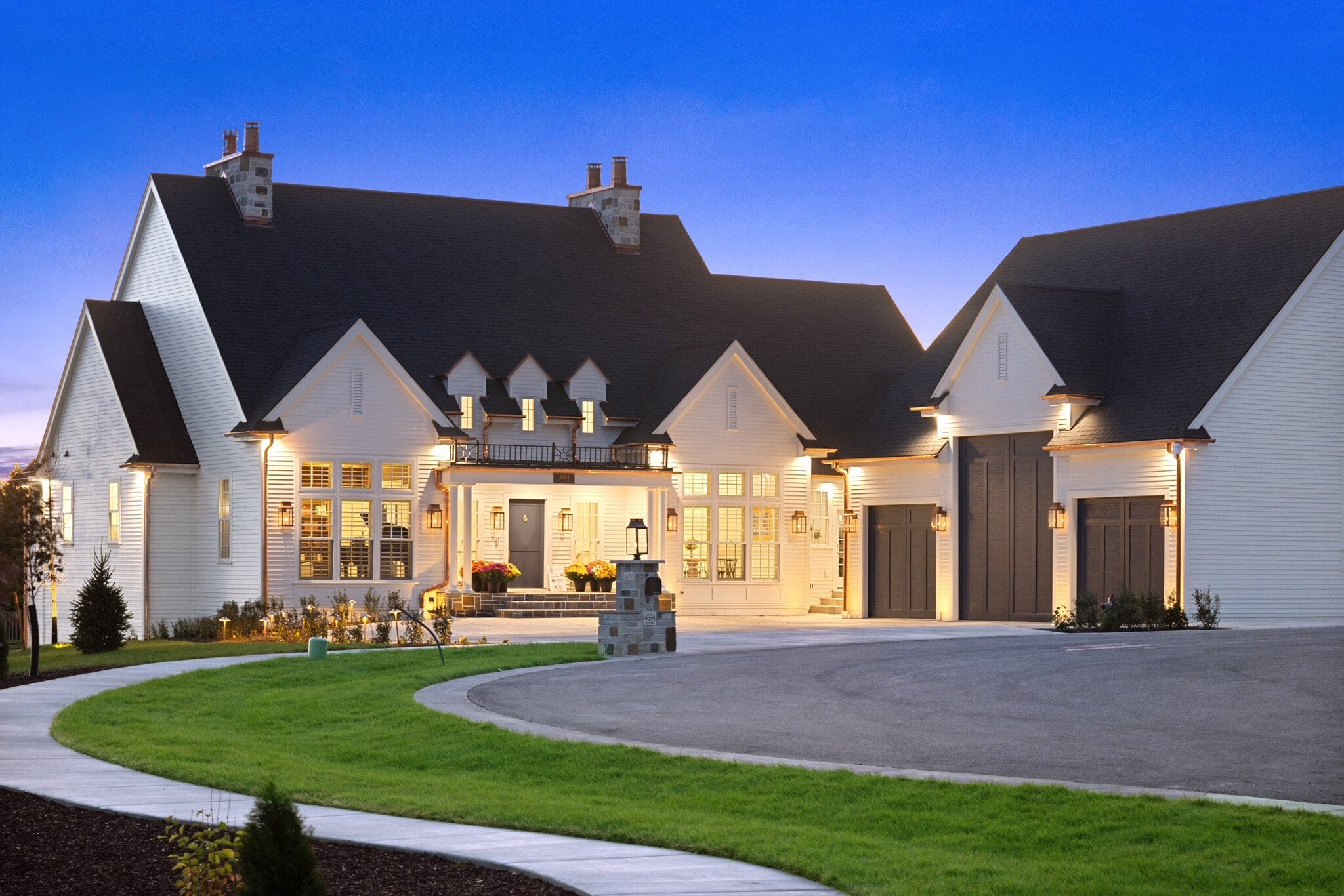 A luxurious modern home with white exterior and well-lit entrance at dusk.