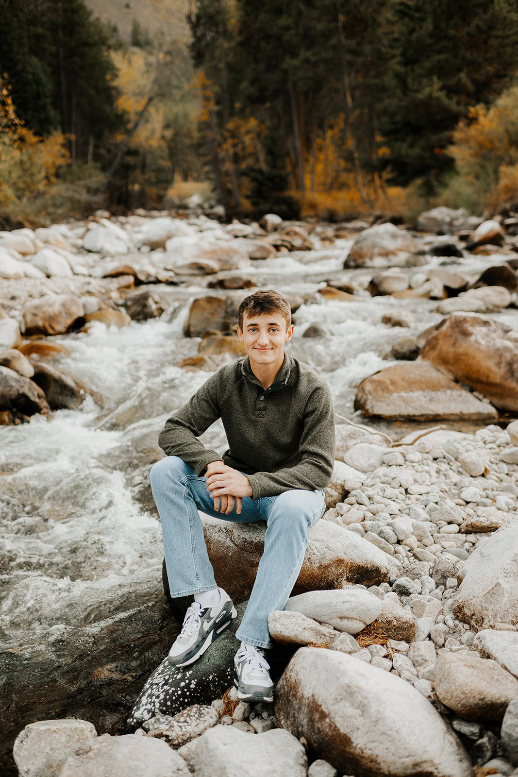Serene young man sitting on rocks by mountain stream in autumn forest.