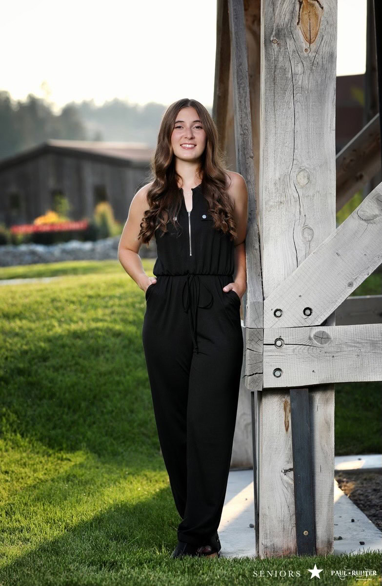 A young woman standing outdoors near a wooden structure, smiling at the camera.